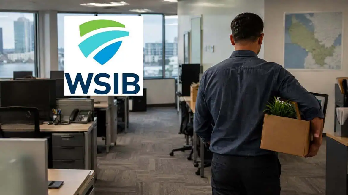 WSIB Job Cuts in Ontario: 466 Positions Affected Across Nine Communities 1 Man holding box in office with WSIB logo on screen.